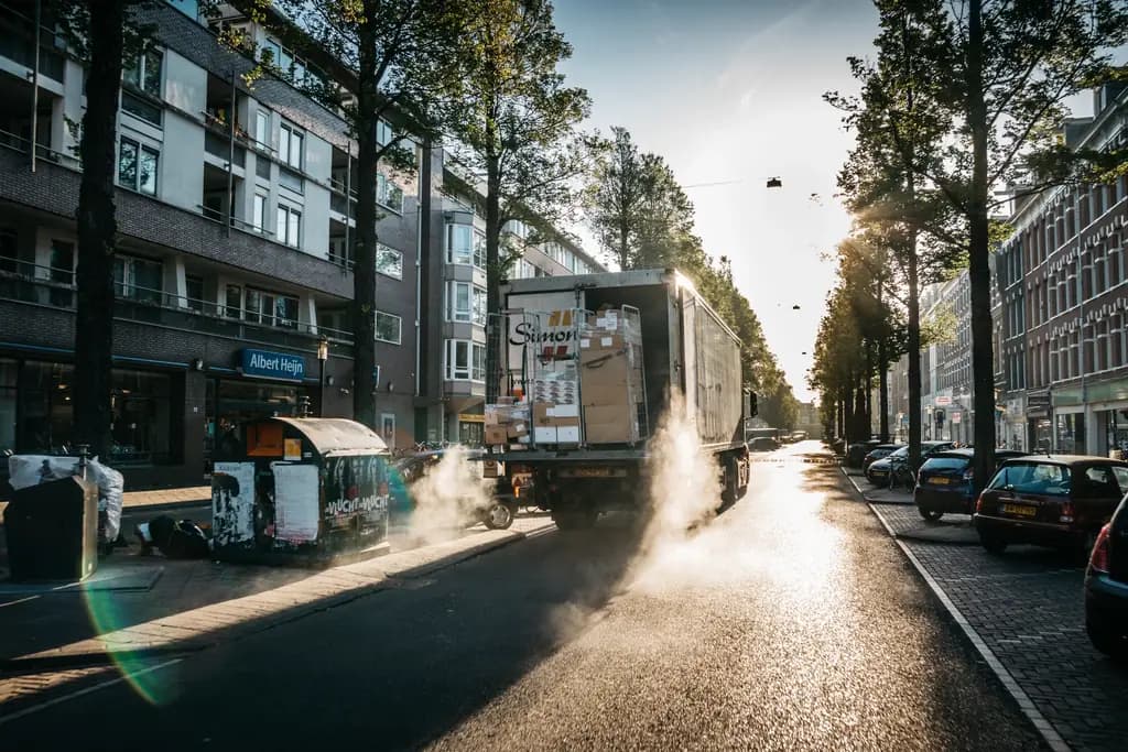 A delivery truck pulling away down a sunlit city street