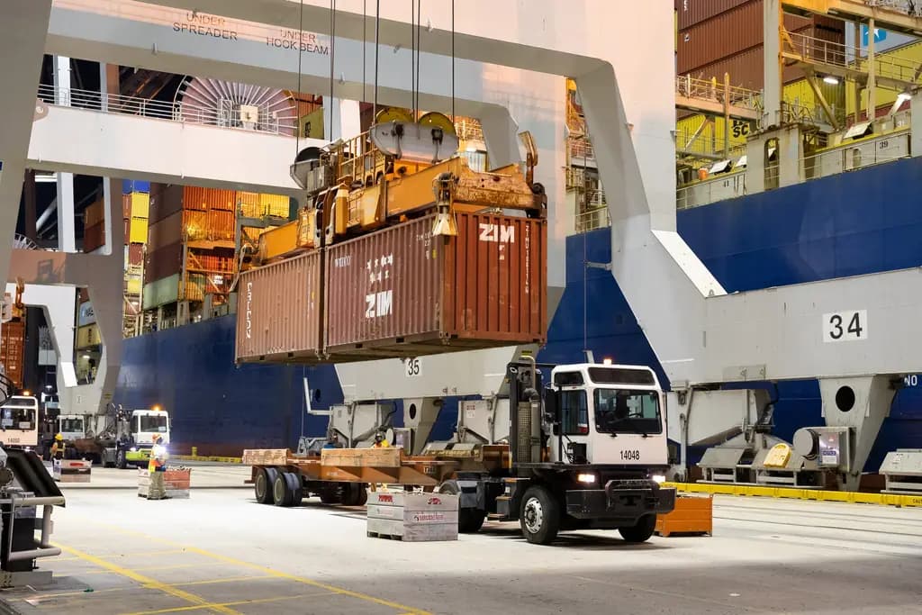 A gantry crane lowering a shipping container onto a waiting truck
